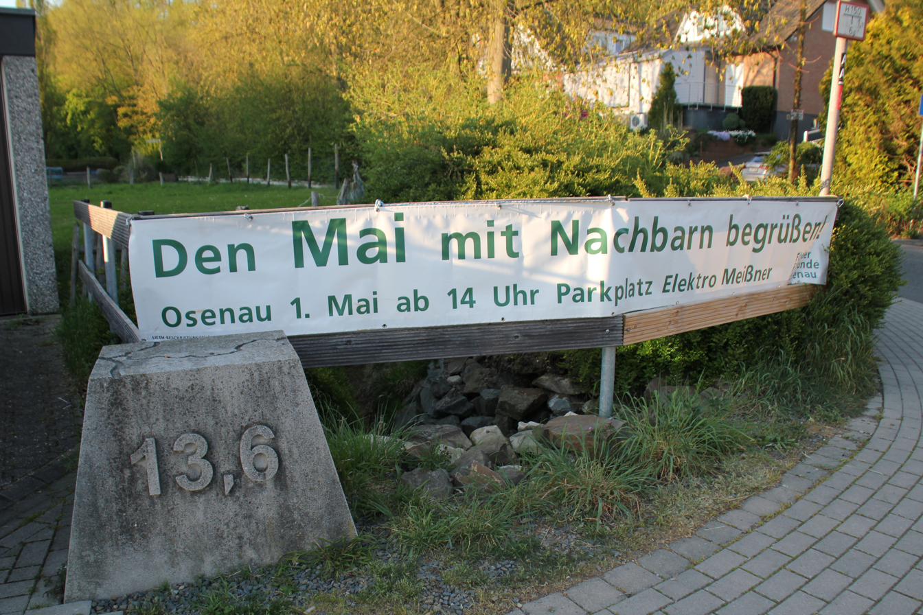 Banner mit dem Schriftzug ‚Den Mai mit Nachbarn begrüßen!‘ am Ortseingang von Osenau.